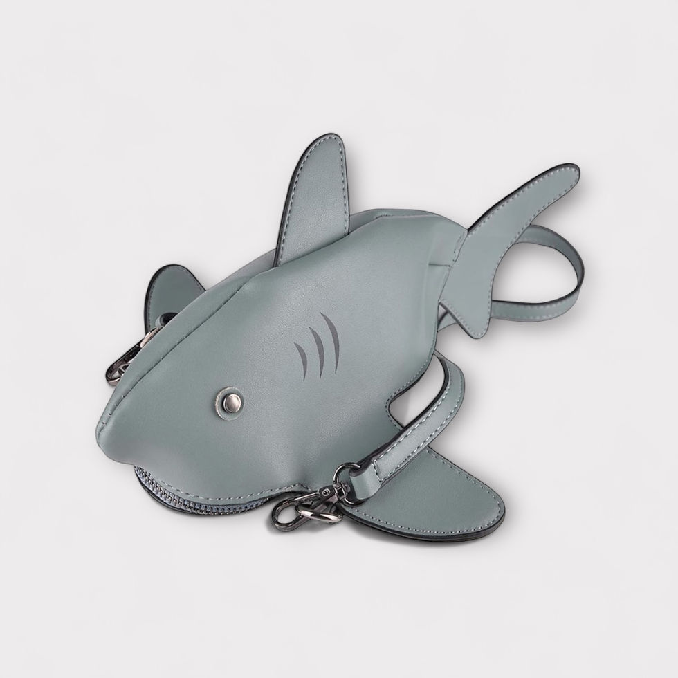 A shark-shaped handbag in light blue-grey with fin details and a zipper mouth rests on a white background, evoking a playful mood.