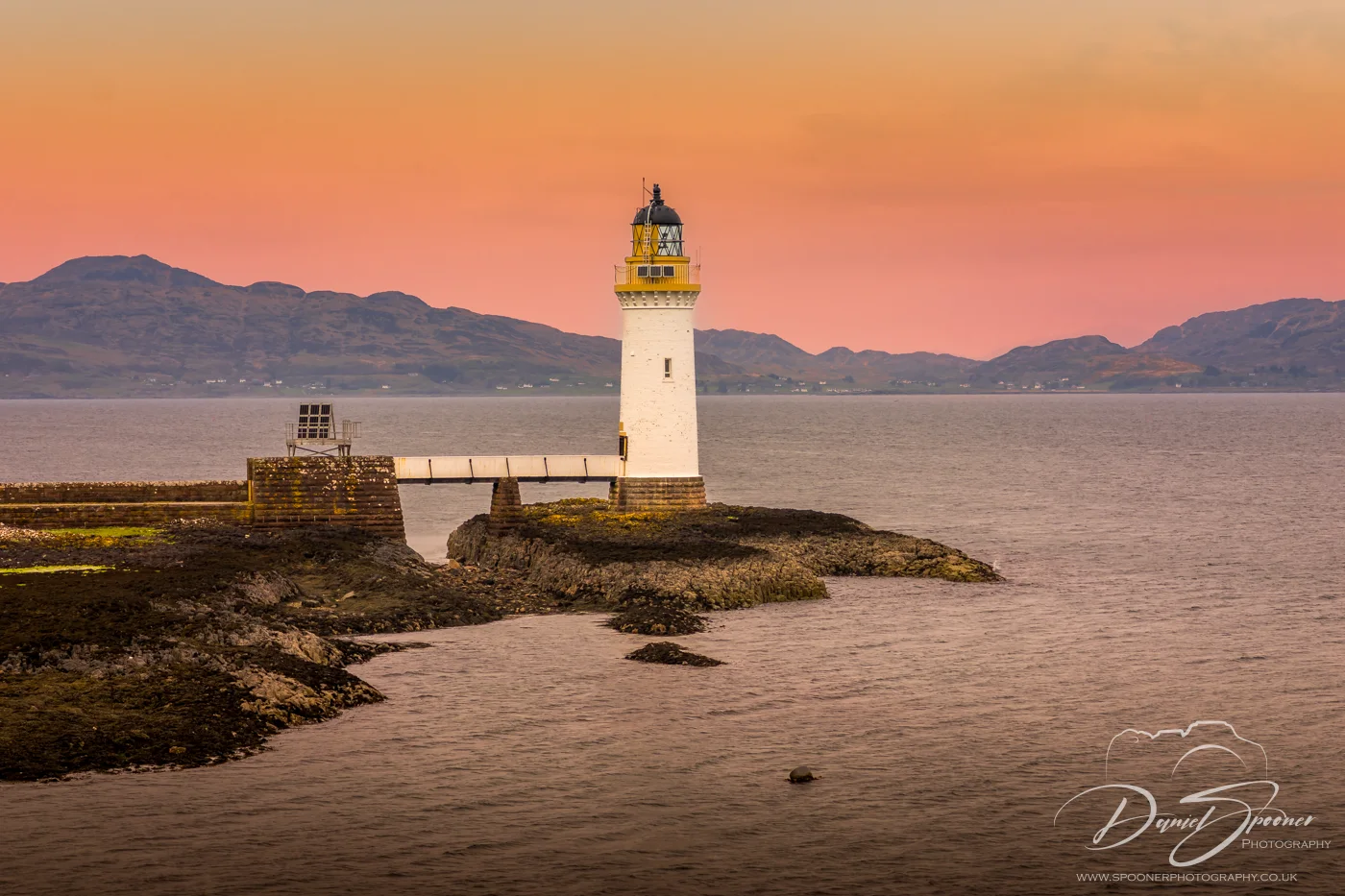 Tobermory Lighthouse at golden hour framed by wild vegetation.