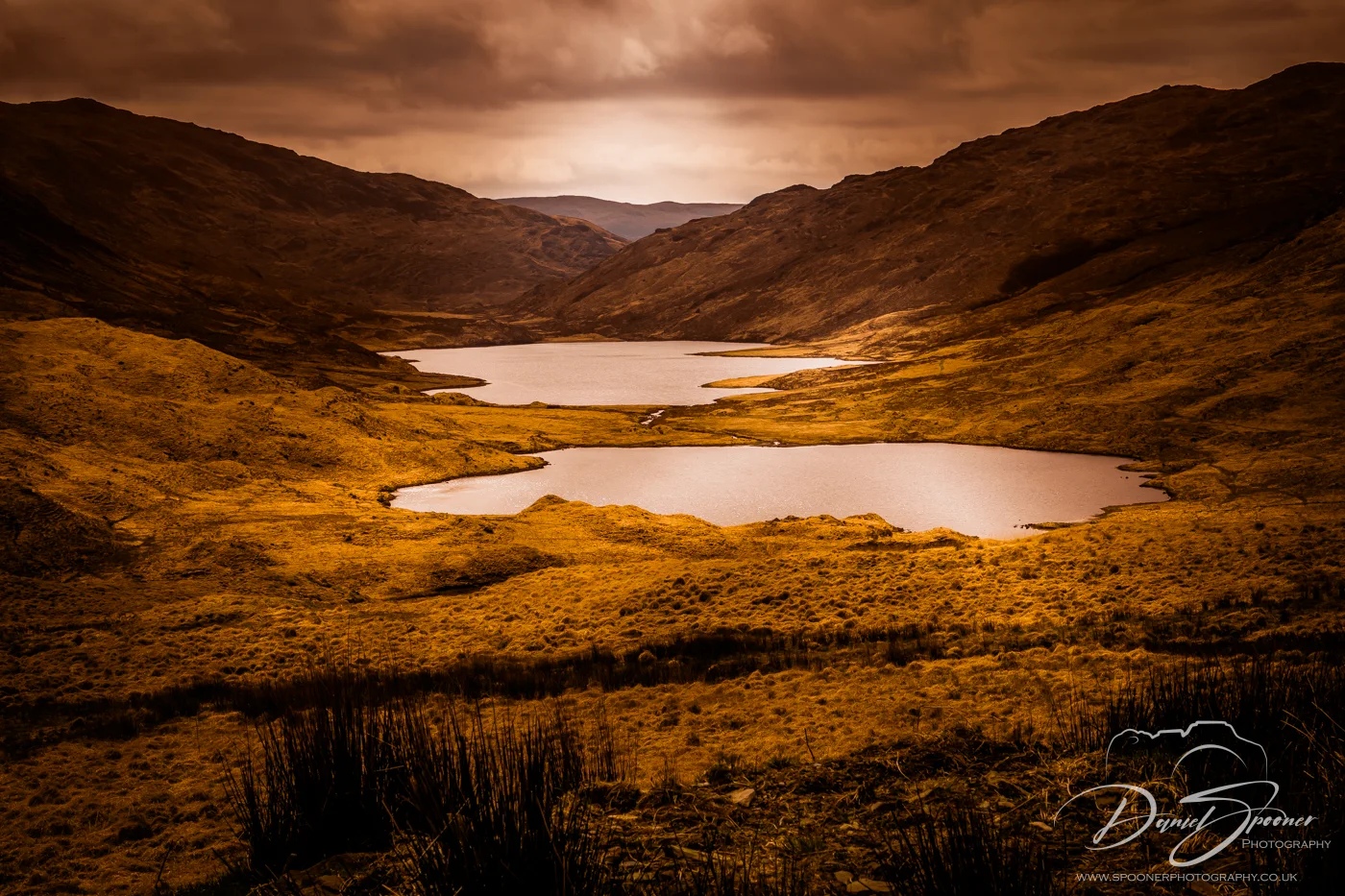 Three shimmering lochs nestled in a golden Highland valley under dramatic overcast skies.