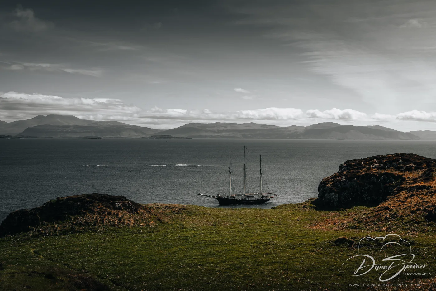 A tall sailing ship anchored in a cove on Lunga Island, surrounded by dramatic cliffs and open sea under moody skies.