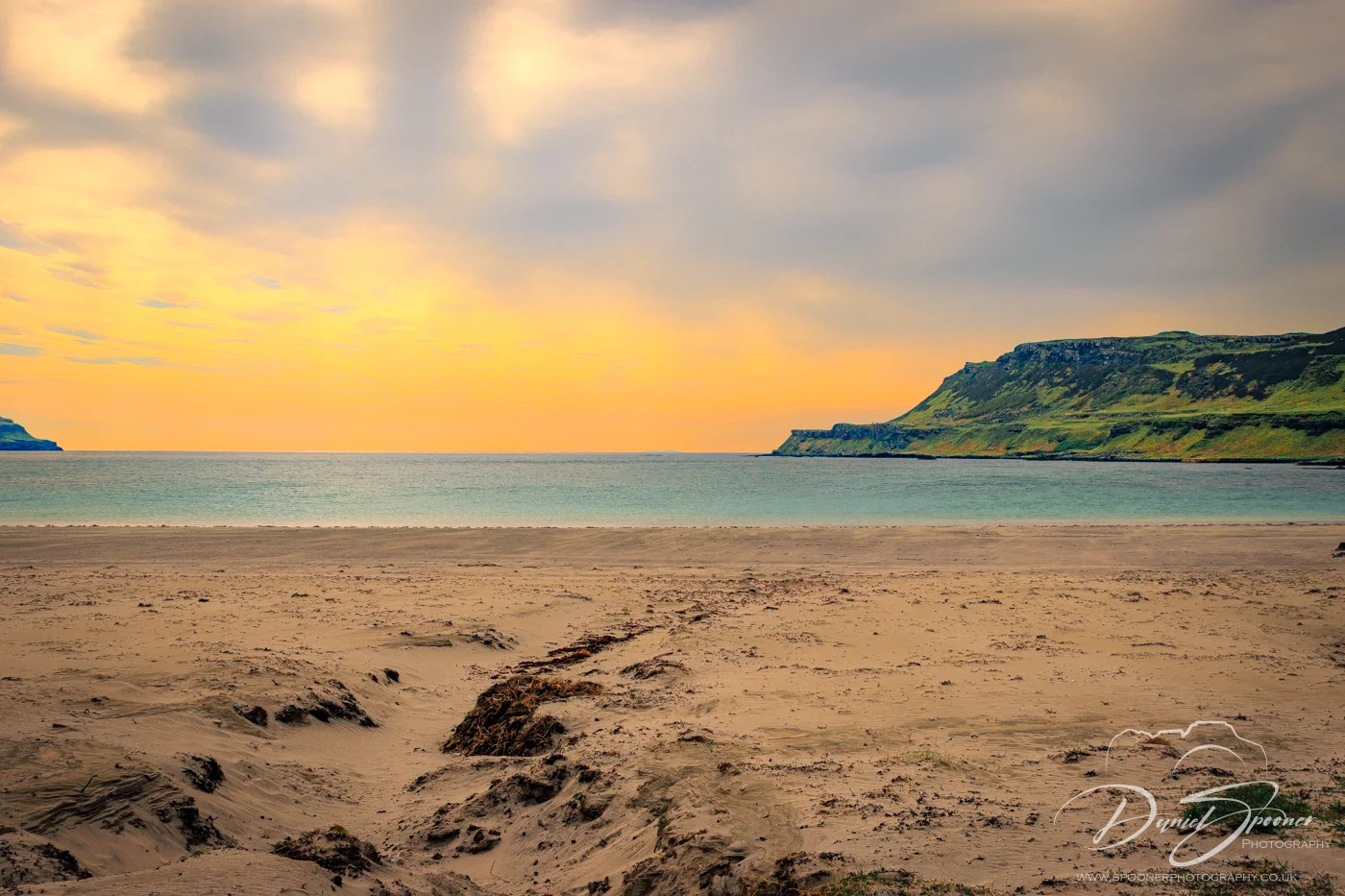 Sunset over Calgary Bay on the Isle of Mull with golden clouds reflecting in the calm sea and rugged cliffs lining the horizon.