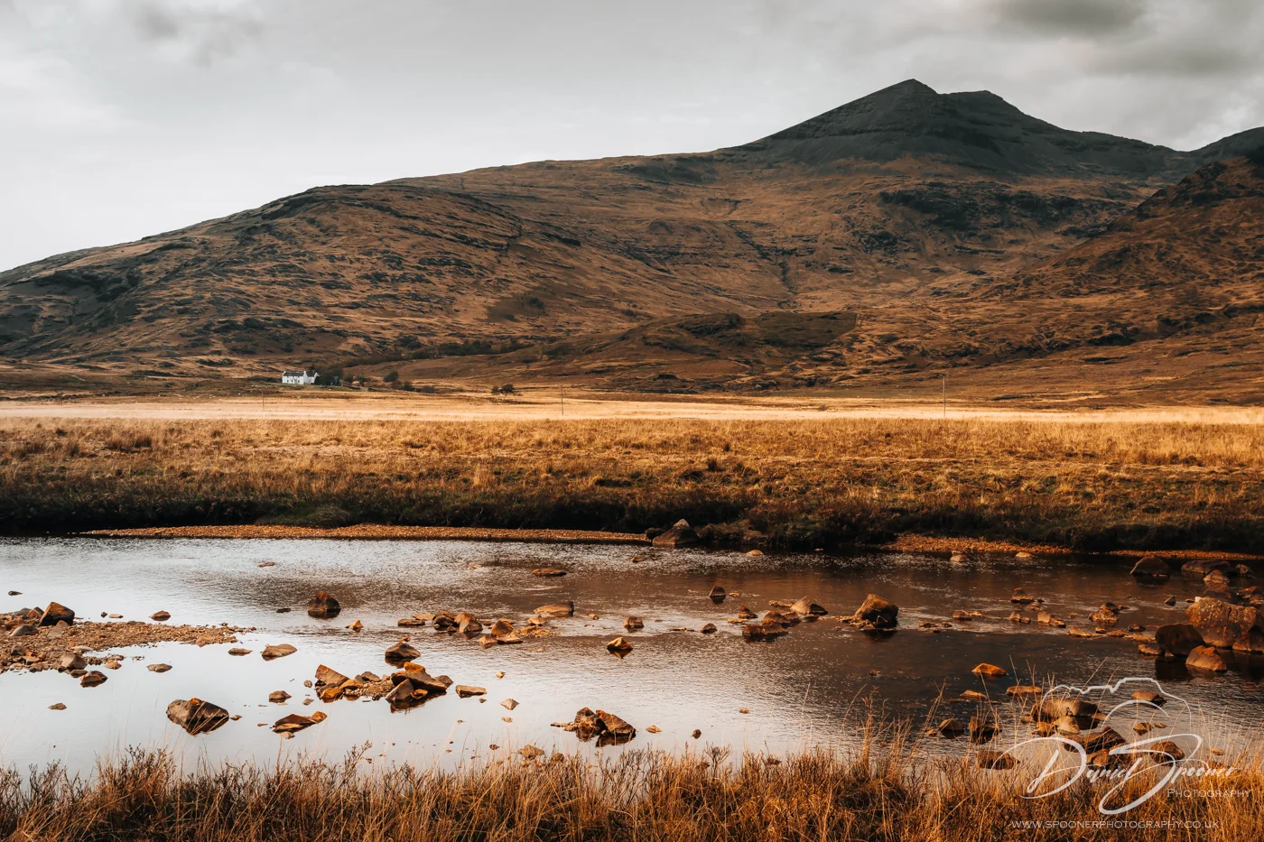 White cottage under golden hills near the peaceful Loch Beg.