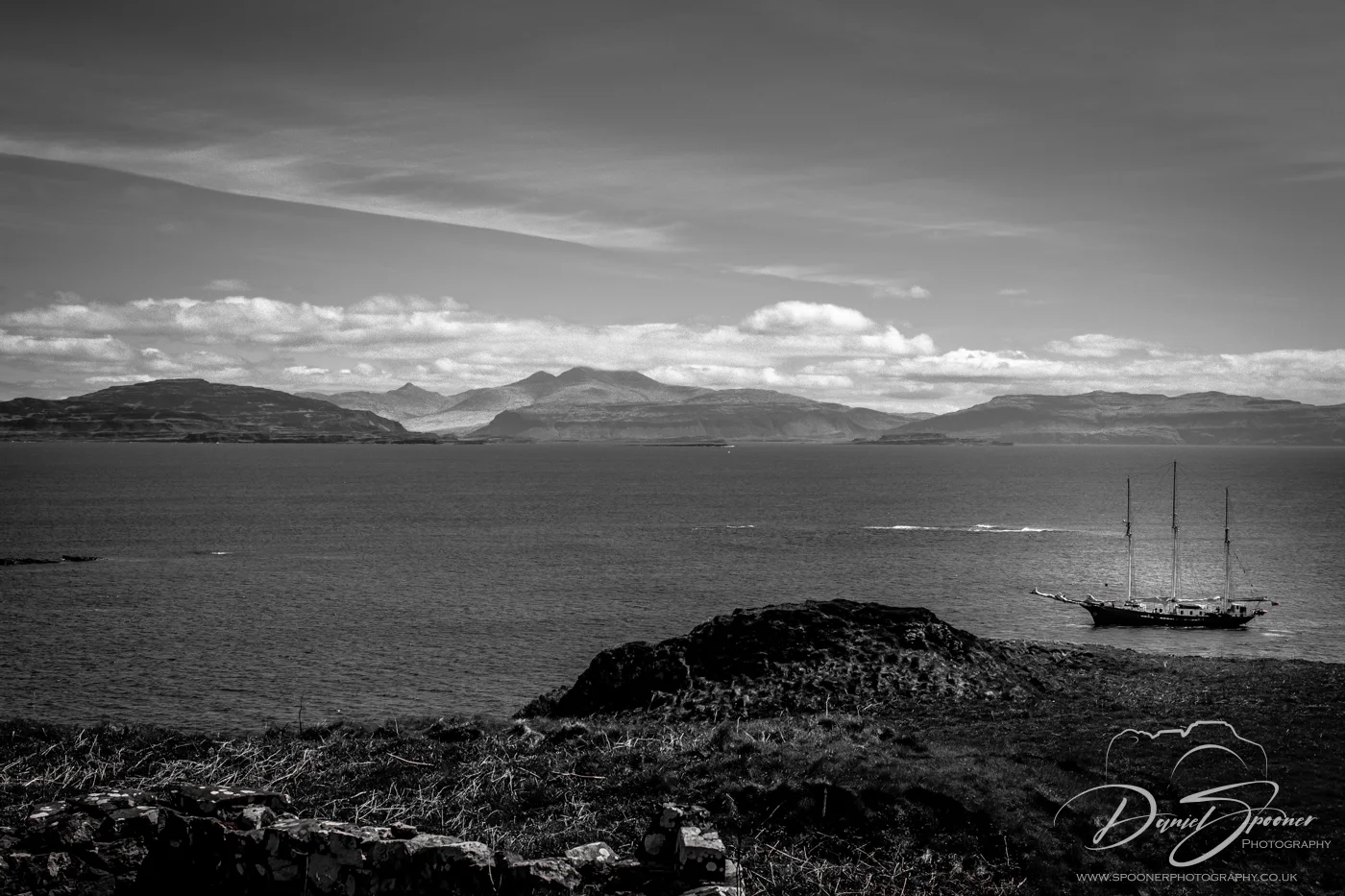 Monochrome view of a sailing ship on the water near Lunga Island, framed by rugged Scottish coastline and distant peaks.