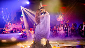 Couple dancing at a wedding reception, surrounded by guests and colorful lights.