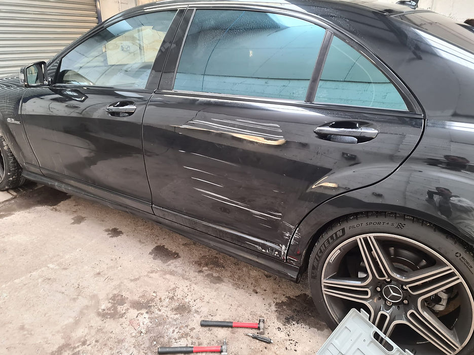 Close up side view of a black car showing minor paint scratches and bodywork damage requiring repair