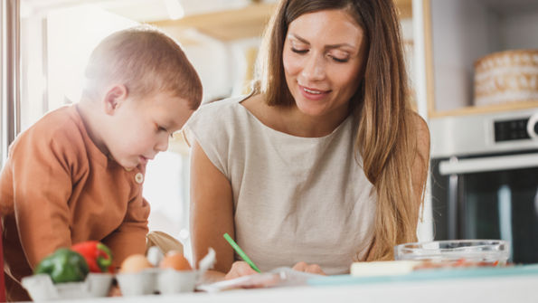 A mother and young child working on schoolwork together at a kitchen table