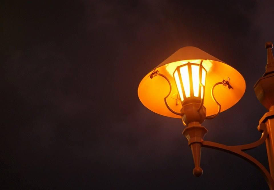 Illuminated street lamp glows against a dark sky, Lisbon, Portugal at dusk.
