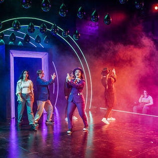 Thrust space. Woman (Sara Jane Moore) seated amongst audience watching The Proprietor (woman in purple suit) give other Assassins their guns. Hands used in lieu of traditional prop guns. Moore admires Zangara, Guiteau, Hinckley and Czolgosz admiring their hand guns