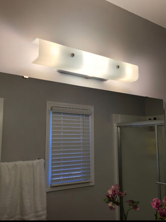 Bathroom vanity light fixture before replacement, featuring the original wall-mounted lighting above the bathroom mirror.