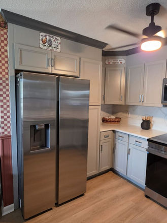 Finished kitchen remodel with gray shaker cabinets, stainless steel refrigerator, quartz countertops, and luxury vinyl plank flooring.