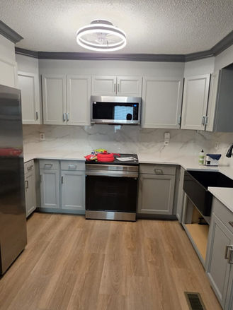 Kitchen renovation featuring gray shaker cabinets, quartz countertops, marble-look backsplash, black farmhouse sink, and stainless steel appliances.