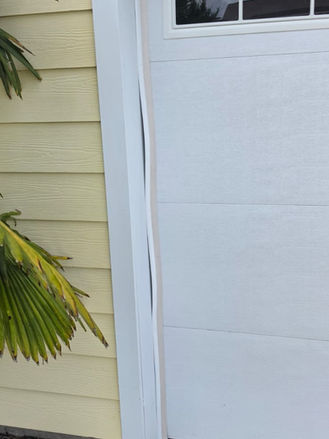 Close-up damaged garage door trim before repair, showing warped and separated exterior trim board.