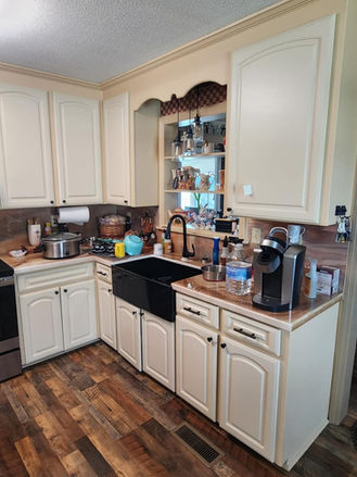Original cream cabinets, black- farmhouse sink, and dark wood-look flooring.