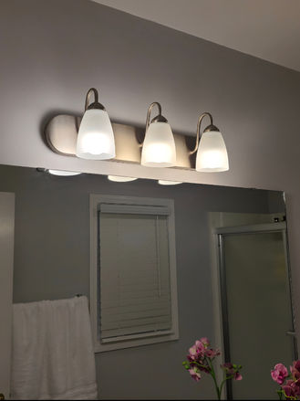 Updated bathroom vanity light fixture with a modern three-light brushed nickel design, improving both style and illumination above the mirror.