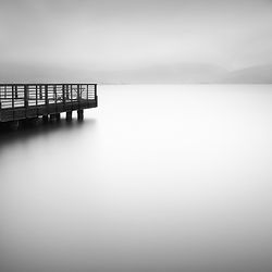 Black and white long exposure photography of pier and lake.