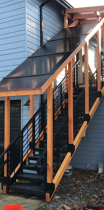 Custom timber-frame lanai roof system built around an existing metal staircase with polycarbonate roofing and custom fabricated matching powder-coated hardware providing covered access to an ADU in Bellingham WA
