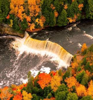 A river with a waterfall surrounded by trees in their fall colors