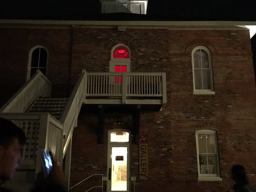 A two-story brick house at night, with a window showing a red light.