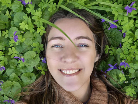 A girl laying in flowering wild violets, smiling. 