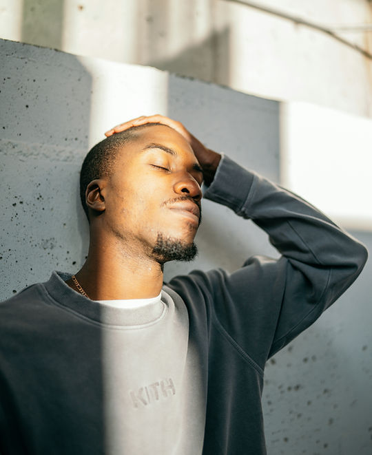 Man leaning against a wall with eyes closed, hand resting on top of head, sunlight on half of his face. Used on PEC FCE landing page to illustrate emotional exhaustion and the collapse of coping. Represents the functional impact of hidden emotional load.