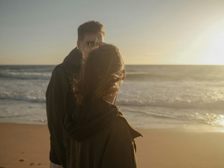 a-man-and-woman-standing-on-a-beach-next-to-the-ocean