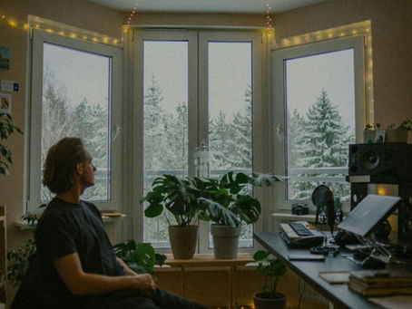 man-sitting-in-a-room-looking-out-at-snowy-trees