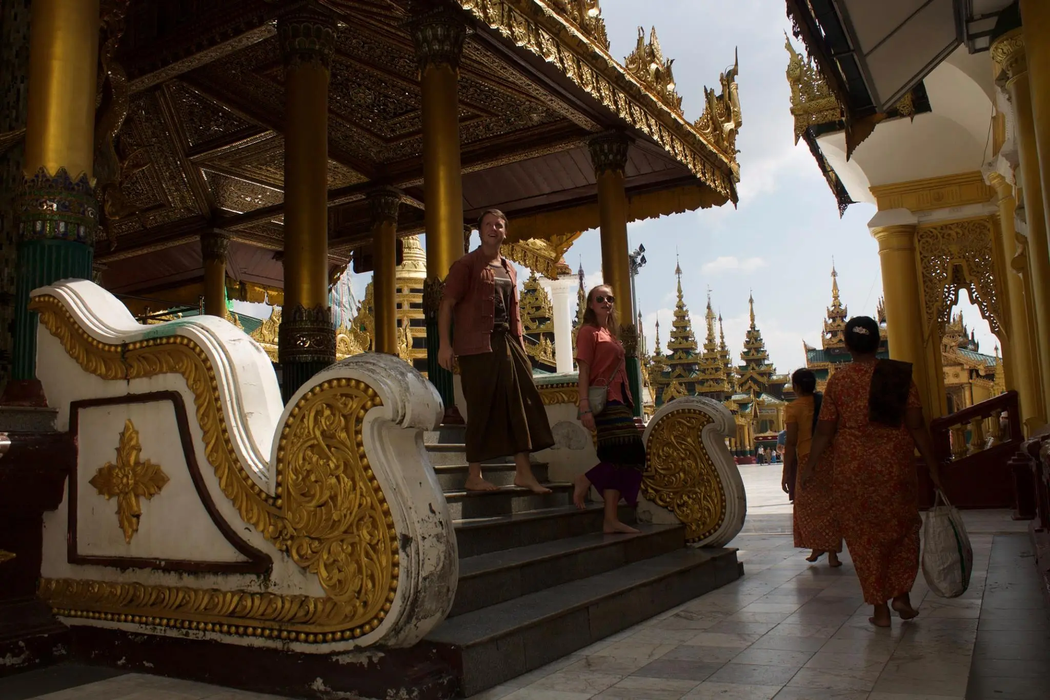 Couple walking down stairs and two women walking away from the camera in a traditional Myanmar Temple. Other temples are seen in the background