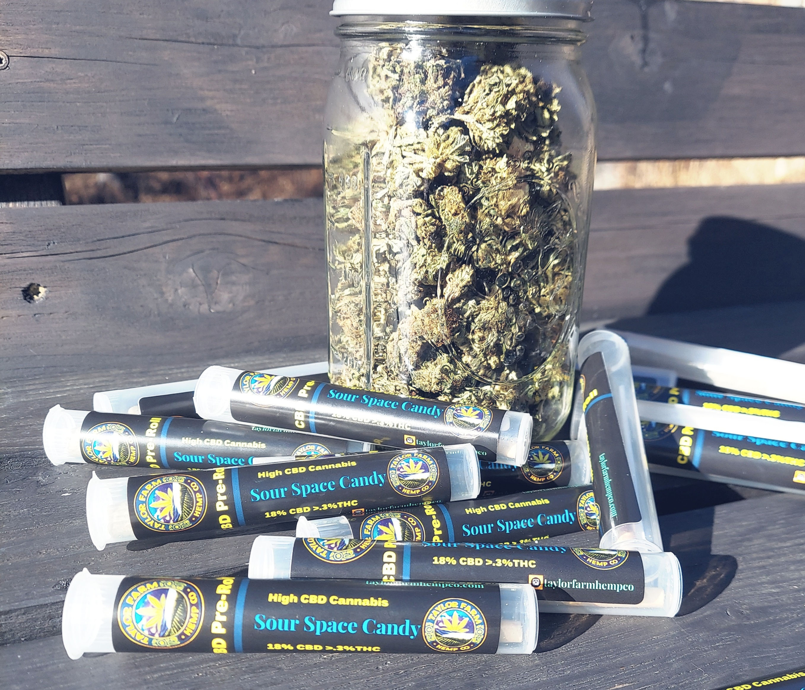 a jar of cbd bud sour space candy surrounded by several tubes of cbd pre-rolls, grown by taylor farm hemp co