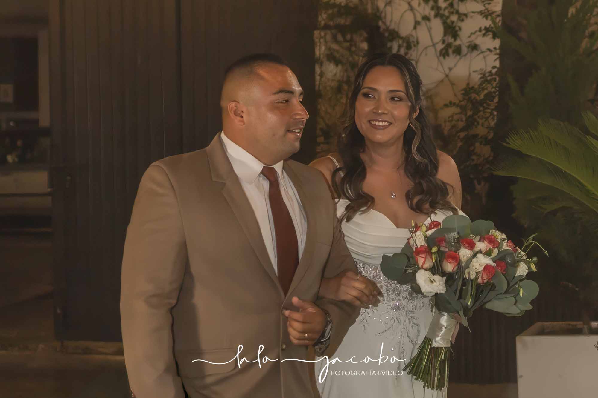 Novios entrando juntos a una celebración nocturna con el logotipo de Lalo Jacobo