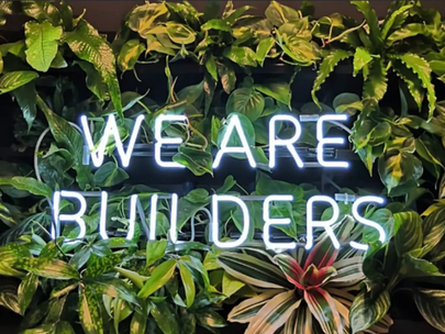 we are builders neon sign on plant wall