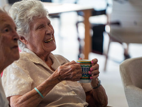 Two older ladies smiling, one with a cup of tea