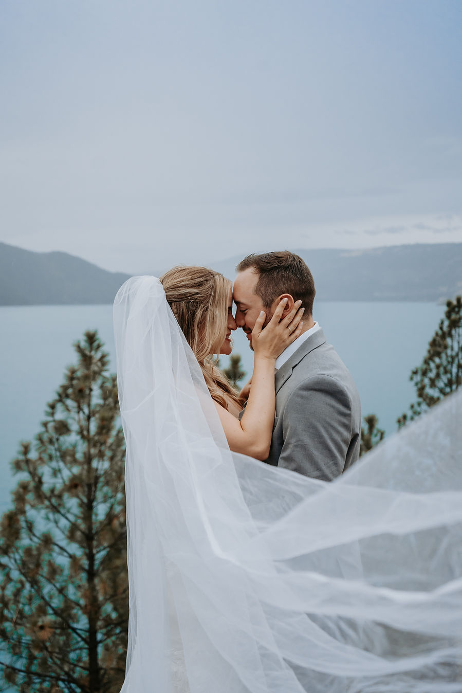 A bride and groom newly married touching noses while overlooking the blue waters of Kalamalka Lake in Vernon, BC, Photographed by Cardinal Vow Media