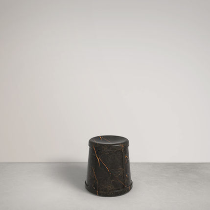 Black marble stool with gold veining against a white wall