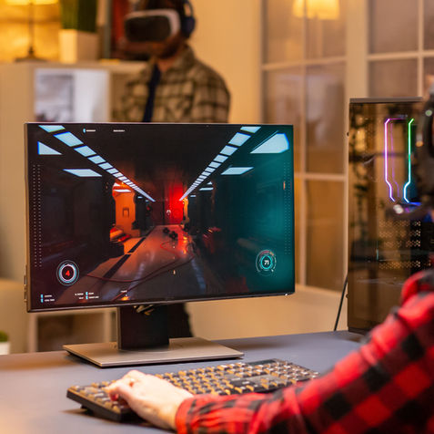 Person playing a video game on a computer in a cosy room with LED lighting and gaming accessories.