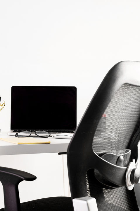 Minimalist workspace with laptop, office chair, desk lamp, and accessories, representing home office and business