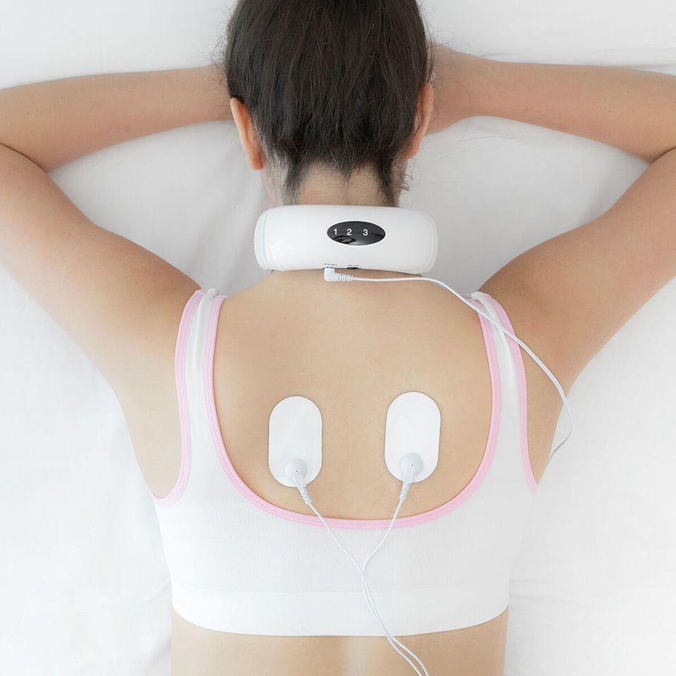 Person wearing a white posture corrector with electronic muscle stimulation pads on the upper back, shown from behind against a neutral background.