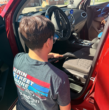Main Street Shine staff vacuums the inside of a customer’s vehicle as part of a full‑service car wash for a cleaner, more comfortable ride.