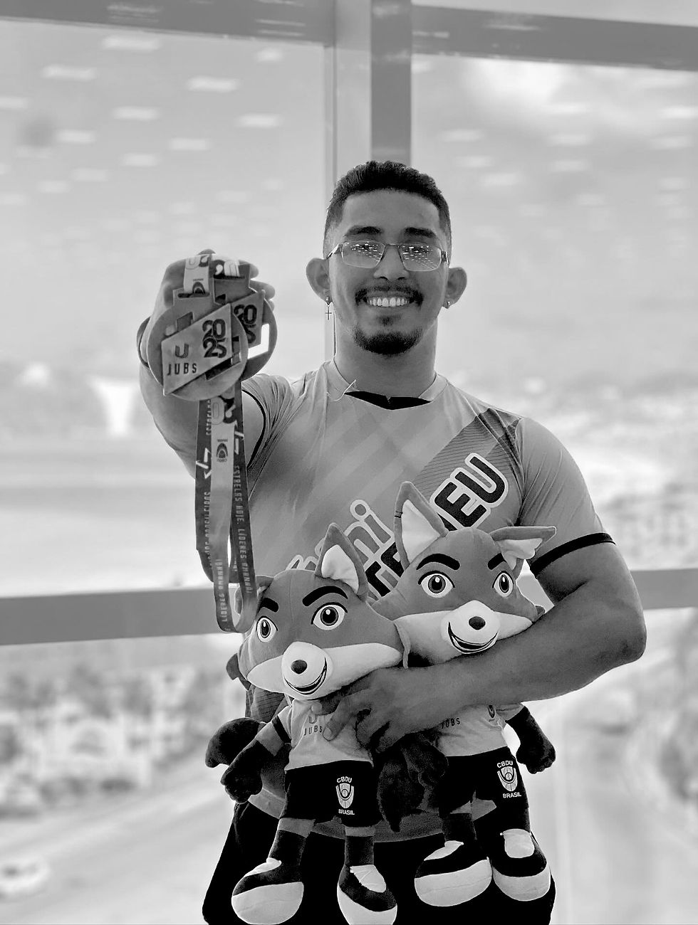 Artur carlos da costa mesquita segurando duas medalhas e dois mascotes de uma competição