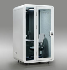 Side-angled view of a white SmartPod Solo Pod Pro soundproof office booth with glass door closed, showing an office chair and desk inside.
