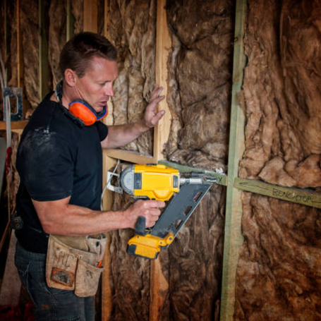 Builder with a nail gun fixing a structural timber stud frame wall.