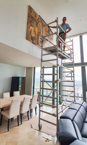 Man standing on scaffolding hanging a large picture | Featured Image for home page for FORWALLS.