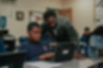Close up of Aurum Prep student using a laptop as a teacher stands next to help while they look at the computer screen together.
