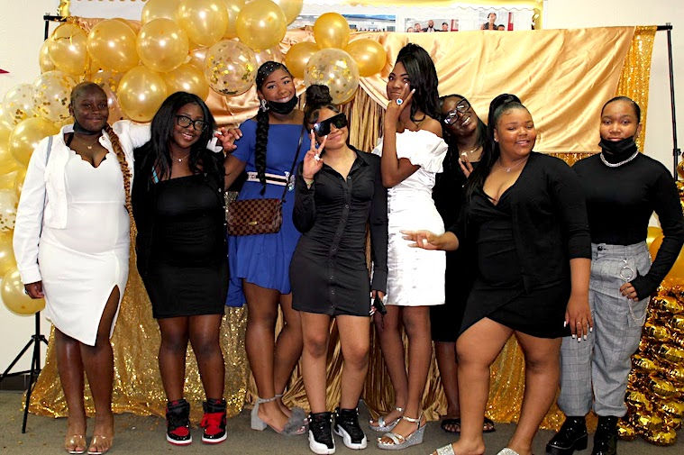 A group of female middle school students from Aurum Preparatory Academy pose for a group photo at the school dance. Decorations include balloons and golden props.