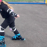 A young child rollerblades on tarmac, wearing bright blue roller blades and a pink helmet.