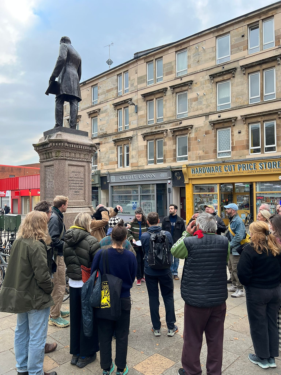 A group of people are on a walking tour - they are standing around a statue in Govan.
