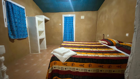 Chambre à coucher avec lit rayé et porte bleue. Photos, Campement Sandugu.