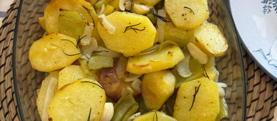 Poor Man’s Potatoes and with herbs in a clear dish on a woven mat. Lemons in a bowl and a glass of water nearby. Cozy setting.