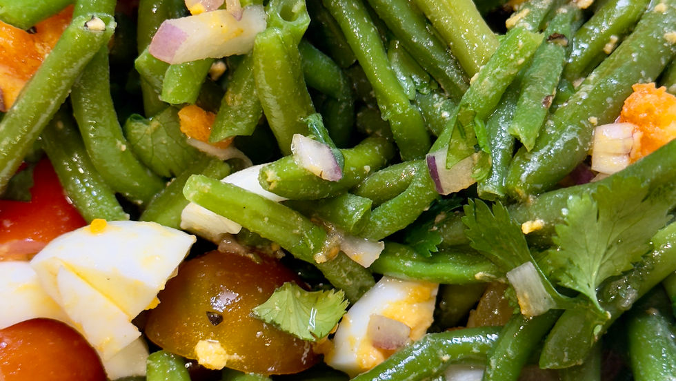 Close-up of a fresh salad with green beans, cherry tomatoes, hard-boiled egg pieces, red onion, and cilantro in a light dressing. Bright colors.