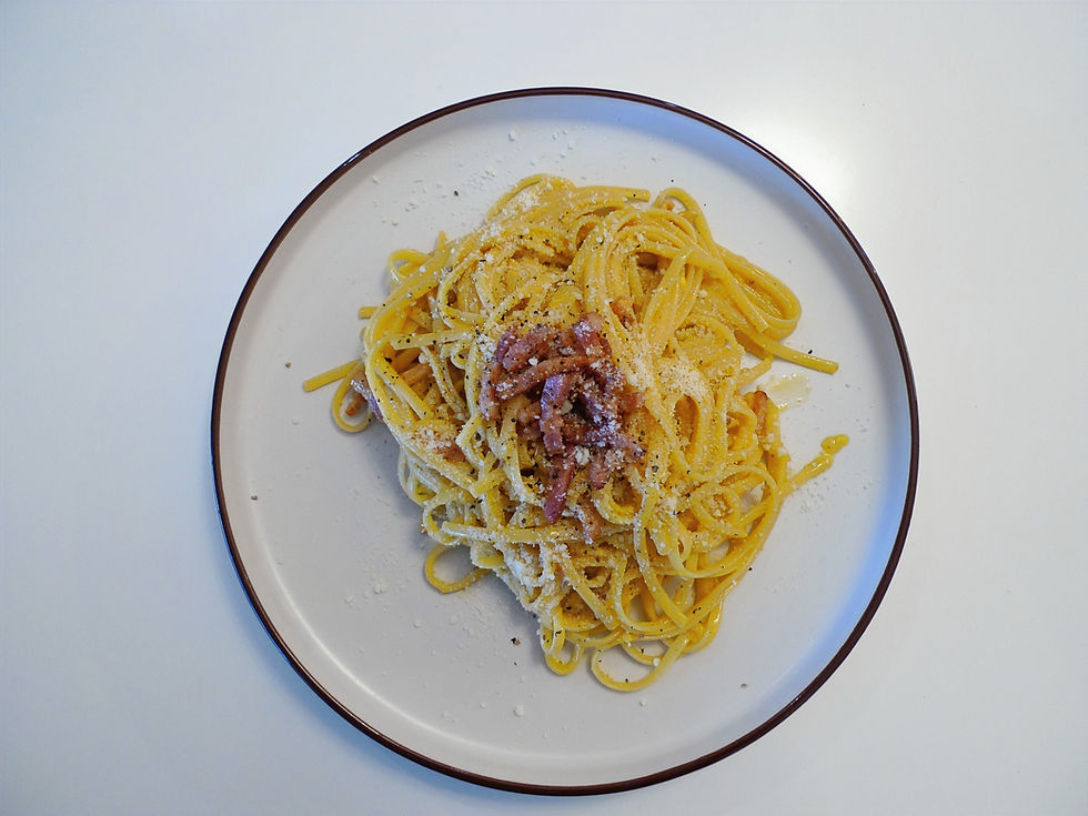 Plate of spaghetti carbonara on a white table. Topped with bacon and grated cheese, creating a savory and appetizing look.