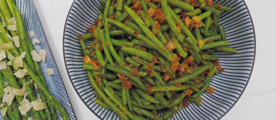 A bowl of green beans with bits of pancetta next to asparagus topped with parmesan on striped dishes, set on a white background.